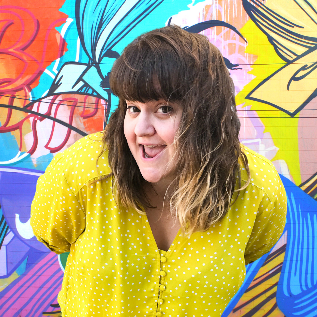 Deanna Seymour in a yellow shirt in front of a colorful graffiti wall.