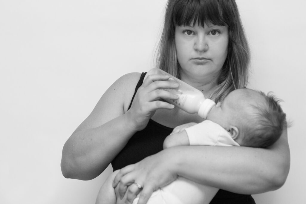 Deanna Seymour stands facing the camera in a black tank top while she bottle feeds her newborn daughter in her arms. She initially felt shame around not breastfeeding as much as she wanted. But eventually embraced that fed is best. Trust us, this relates to your content plan. 