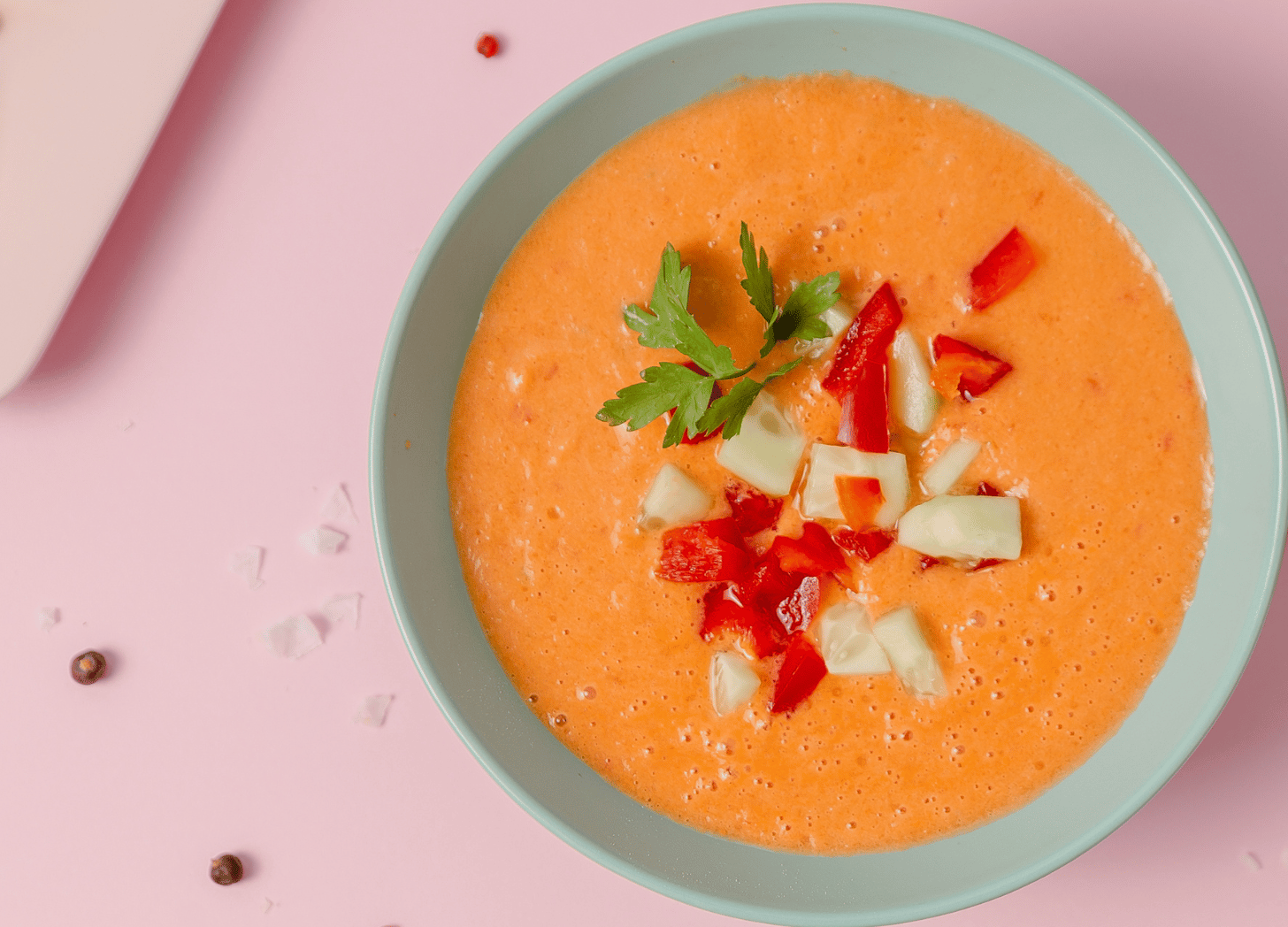 Gazpacho soup with tomato and onions and parsley on top in a blue bowl on a pink table